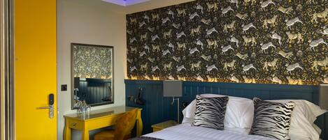 A hotel room with a zebra-patterned bedspread, a desk with a chair, a mirror, and a wall with a patterned wallpaper.