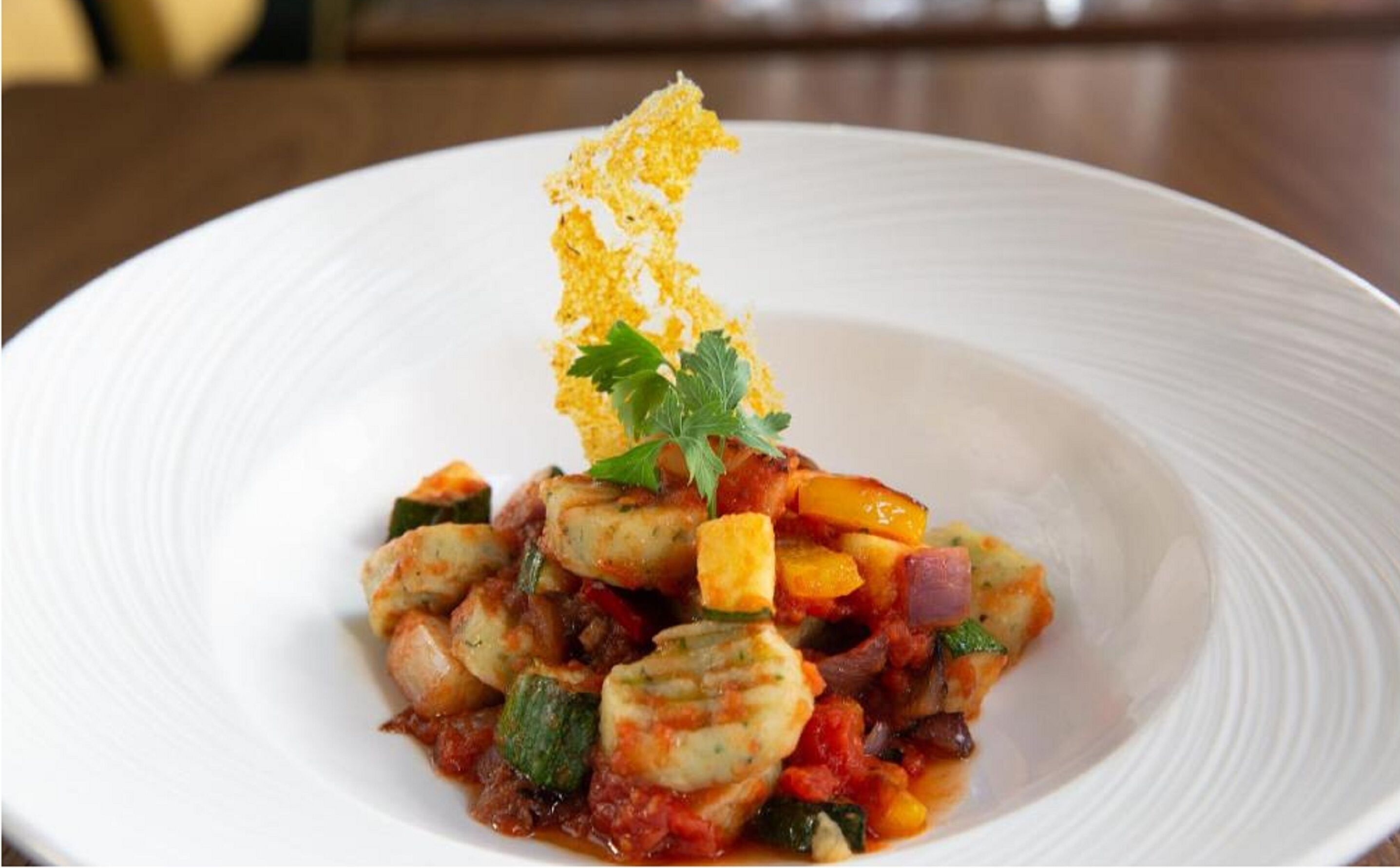 Une assiette blanche contenant un plat de fruits de mer, notamment des crevettes et des légumes, garni de persil et d'un élément croustillant.