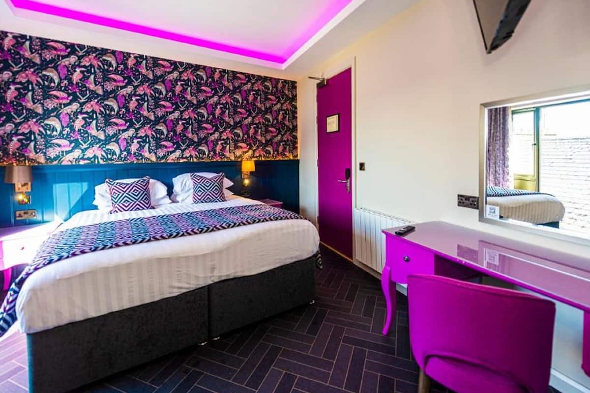 A modern bedroom with a bed, desk, and chair, featuring vibrant wallpaper and a window with a view.
