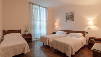 Une chambre d’hôtel avec deux lits simples, un plancher en bois, une fenêtre avec des rideaux légers, une table de chevet avec une lampe et un tableau au mur.