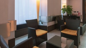 A modern lounge area with wicker furniture, a glass table, and a large window with sheer curtains. - Hotel Bologna (Turin)