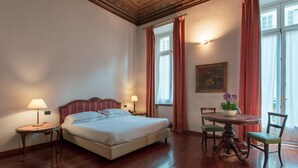 A hotel room with a bed, two bedside tables, a round table with chairs, a window with curtains, and a painting on the wall. - Hotel Bologna (Turin)