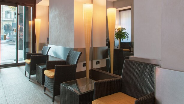 A hotel lobby with wicker furniture, a glass table, and a large mirror. - Hotel Bologna (Turin)