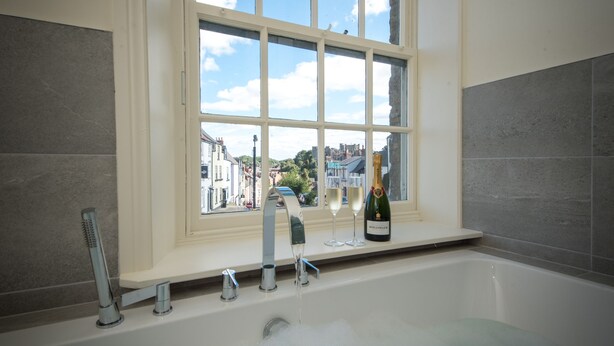 A bathroom with a bathtub, a window, and a bottle of champagne. - Toast Lettings | Crossgate, 2 bedroom Durham City cottage with castle views (Saint Margarets Garth)