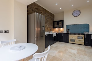 A modern kitchen with a stone accent wall, stainless steel appliances, and a blue backsplash. - Toast Lettings | Crossgate, 2 bedroom Durham City cottage with castle views (Saint Margarets Garth)