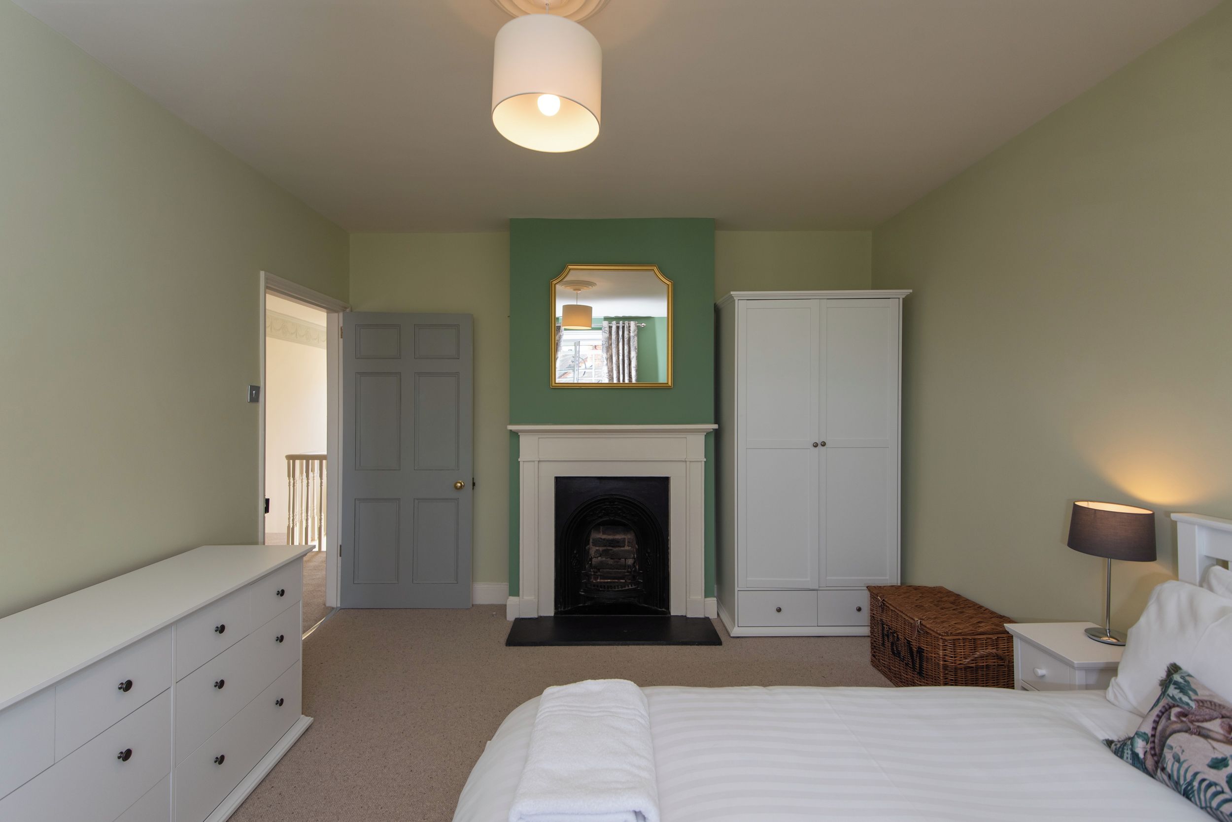 A bedroom with a bed, dresser, wardrobe, fireplace, and a mirror.