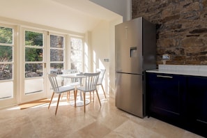 Una cocina moderna con refrigerador integrado, pared de piedra y comedor con sillas blancas y una mesa.