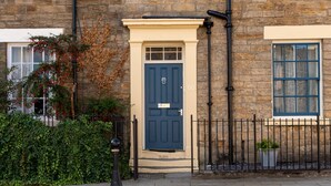 A stone building with a dark blue door, a number 50 sign, and a small garden area with a fence and potted plants. - Toast Lettings | Crossgate, 2 bedroom Durham City cottage with castle views (Saint Margarets Garth)