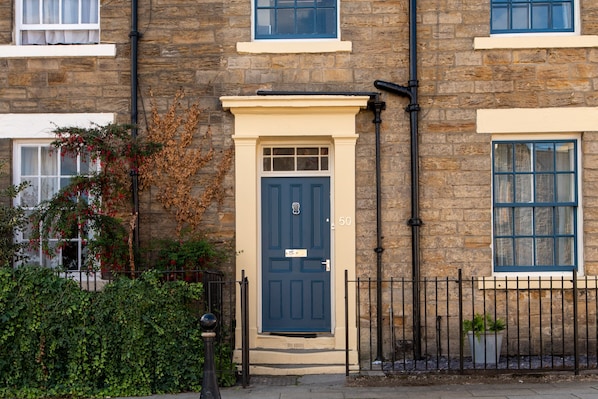 A stone building with a dark blue door, a number 50 sign, and a small garden area with a fence and potted plants. - Toast Lettings | Crossgate, 2 bedroom Durham City cottage with castle views (Saint Margarets Garth)