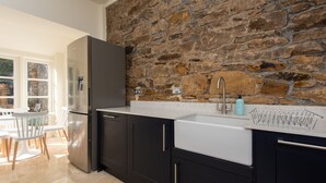A modern kitchen with dark cabinets, a white sink, and a stone wall backsplash. - Toast Lettings | Crossgate, 2 bedroom Durham City cottage with castle views (Saint Margarets Garth)