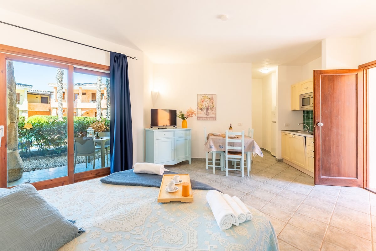 A hotel room with a bed, a small desk, a dining table, and a kitchen area.