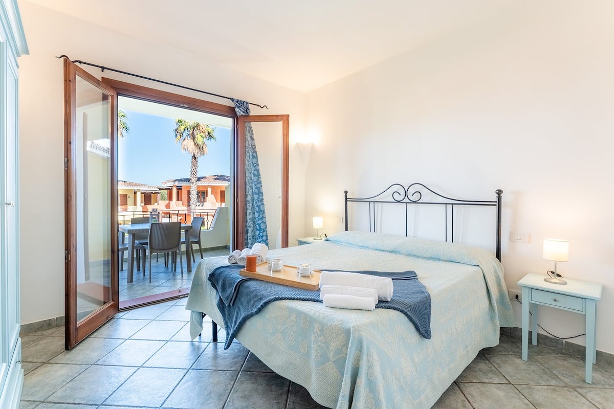 A bedroom with a bed, a bedside table, and a view of an outdoor patio.