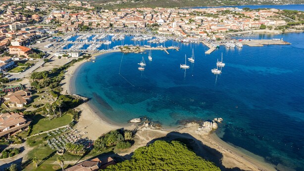 Vista aèria d'una població costanera amb un port esportiu, platges de sorra i edificis residencials.