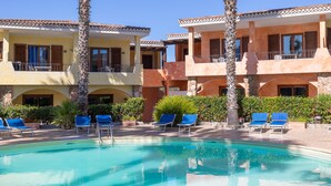 Zona de piscina amb gandules i una piscina blava i cristal·lina, envoltada d'edificis d'àmbit elevat amb balcons i palmeres.
