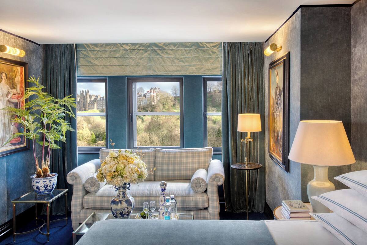 A room with a large window, a sofa, a table with a vase of flowers, and a lamp.