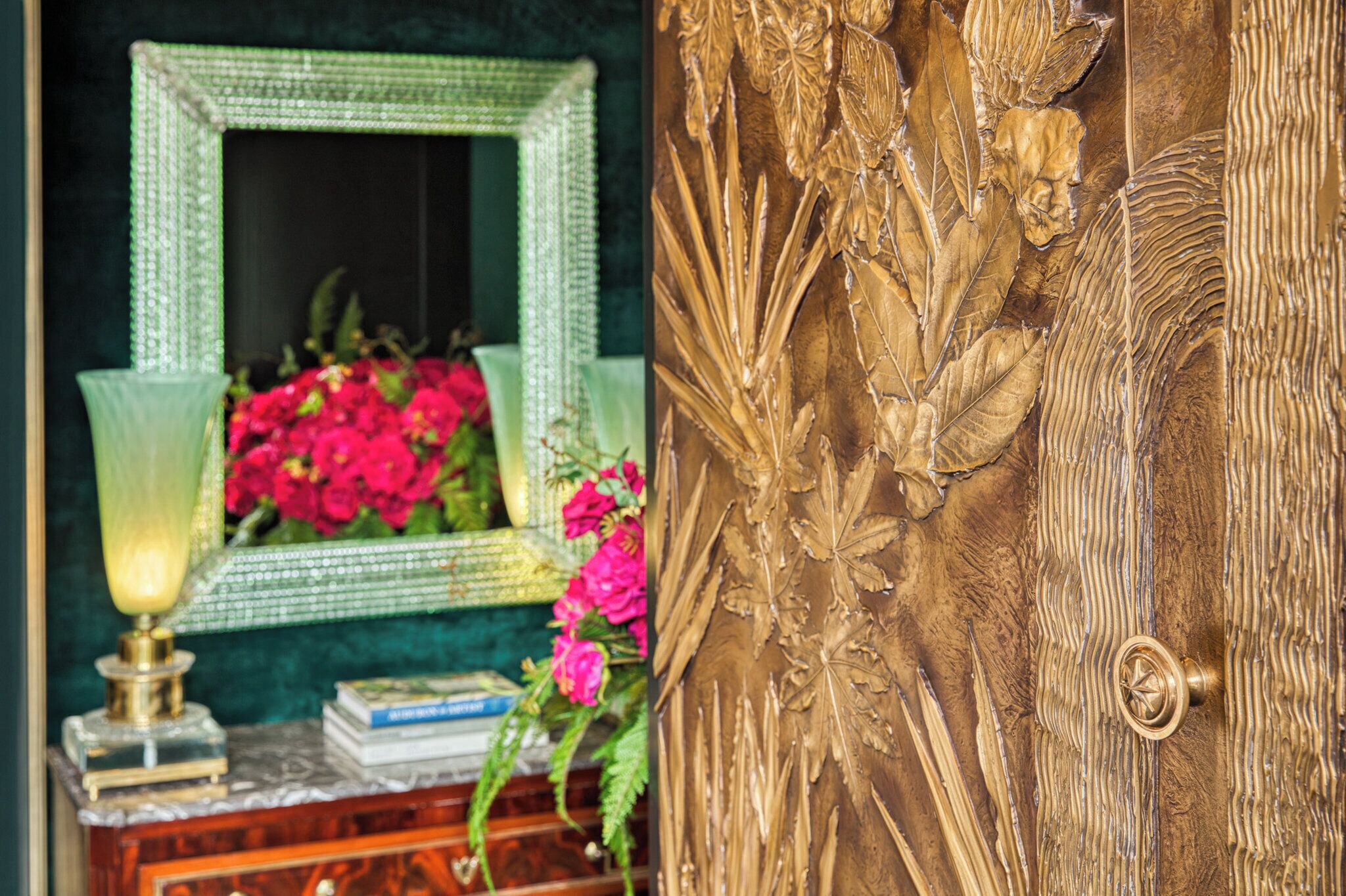 A room with a green mirror, a lamp, and a floral arrangement.