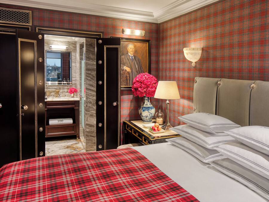 A hotel room with a bed, a nightstand, a lamp, a vase with flowers, a mirror, and a wardrobe.