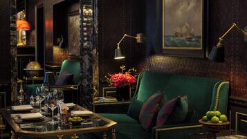 Ein luxuriöses Zimmer mit einem grünen Sofa, einem gedeckten Esstisch mit Gläsern und einer Blumenvase, sowie einem Gemälde eines Schiffes an der Wand.