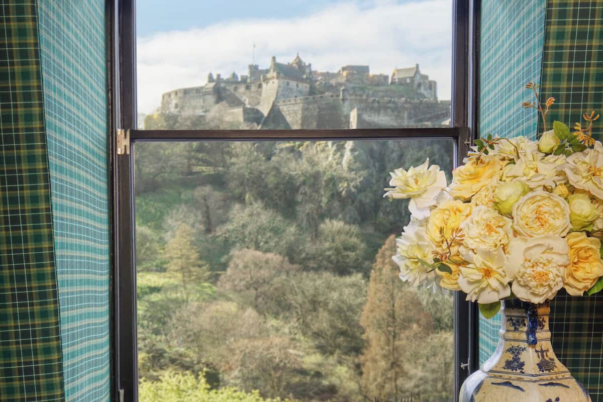 A window with a view of a historic castle and a vase of flowers.