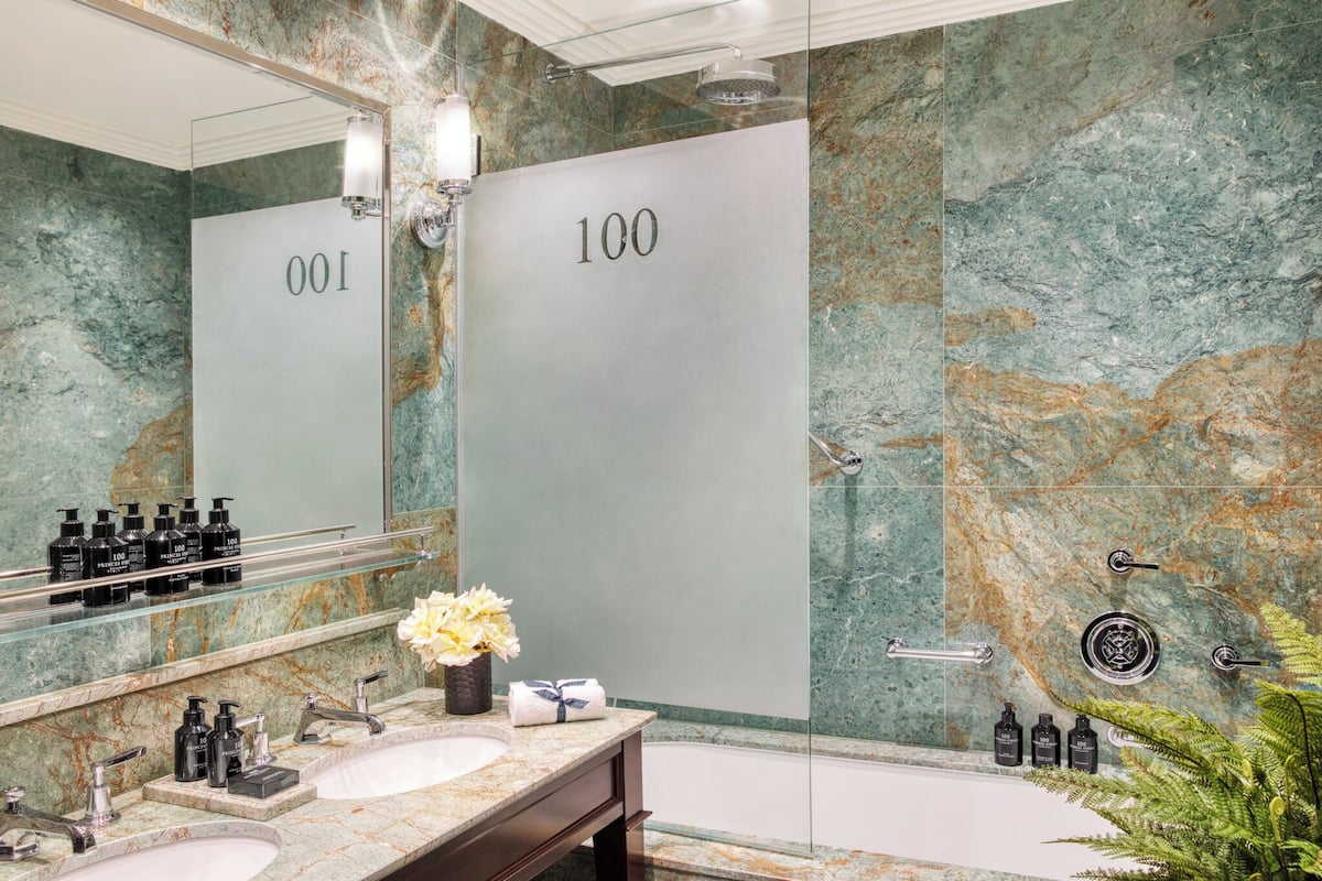 A bathroom with a marble wall, a large mirror, a sink with toiletries, and a bathtub.