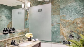 A bathroom with a marble wall, a large mirror, a sink with toiletries, and a bathtub.