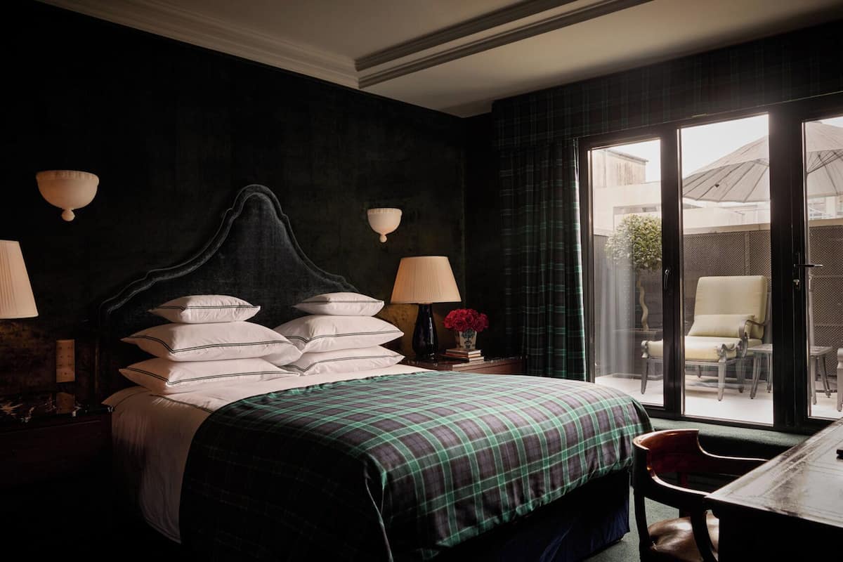 A hotel room with a large bed, two bedside lamps, a window with a view of the outside, and a small table with a chair.