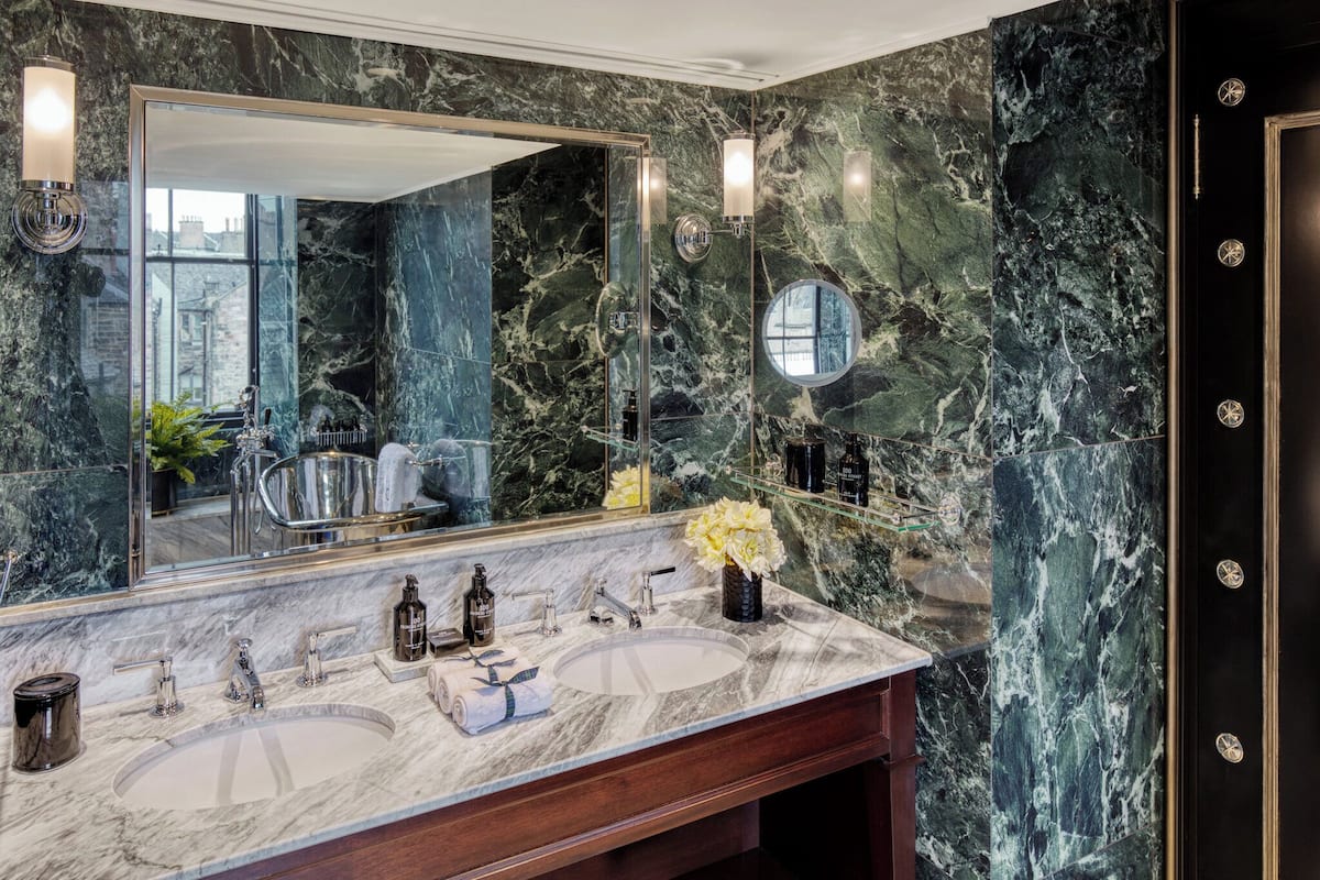 A bathroom with a marble vanity, two sinks, a large mirror, and a view of the city through the window.