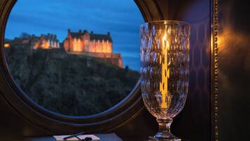 A view of a castle through a window, a glass table with a candle, and a leather-bound book.