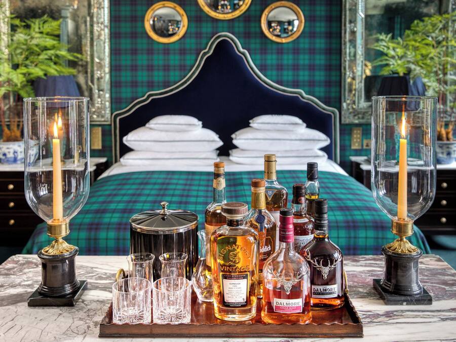 Une chambre à coucher luxueuse avec un grand lit, un plateau rempli de bouteilles d’alcool et des chandeliers.