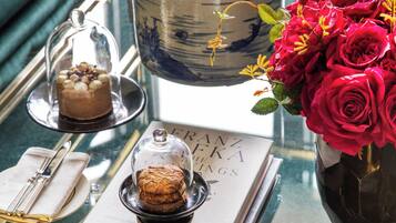 Una mesa con un libro, una campana de cristal sobre un postre, un jarrón con rosas rojas y una maceta de cerámica.