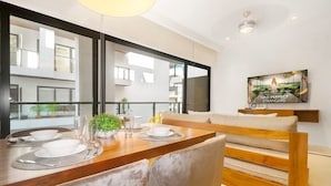 A modern dining area with a wooden table set for two, a bench, and a large window offering a view of the building's exterior. - 1BR Ocean View, Gym & Rooftop Bar! (Playa del Carmen)