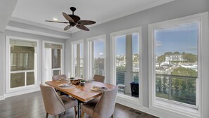A dining room with a wooden table, six chairs, and a ceiling fan. Large windows offer a view of the city. - Award-Winning Resort Amenities | Yacht Harbor Court 31 (Isle of Palms)