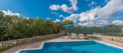 A swimming pool with a stone wall and a covered area with lounge chairs.