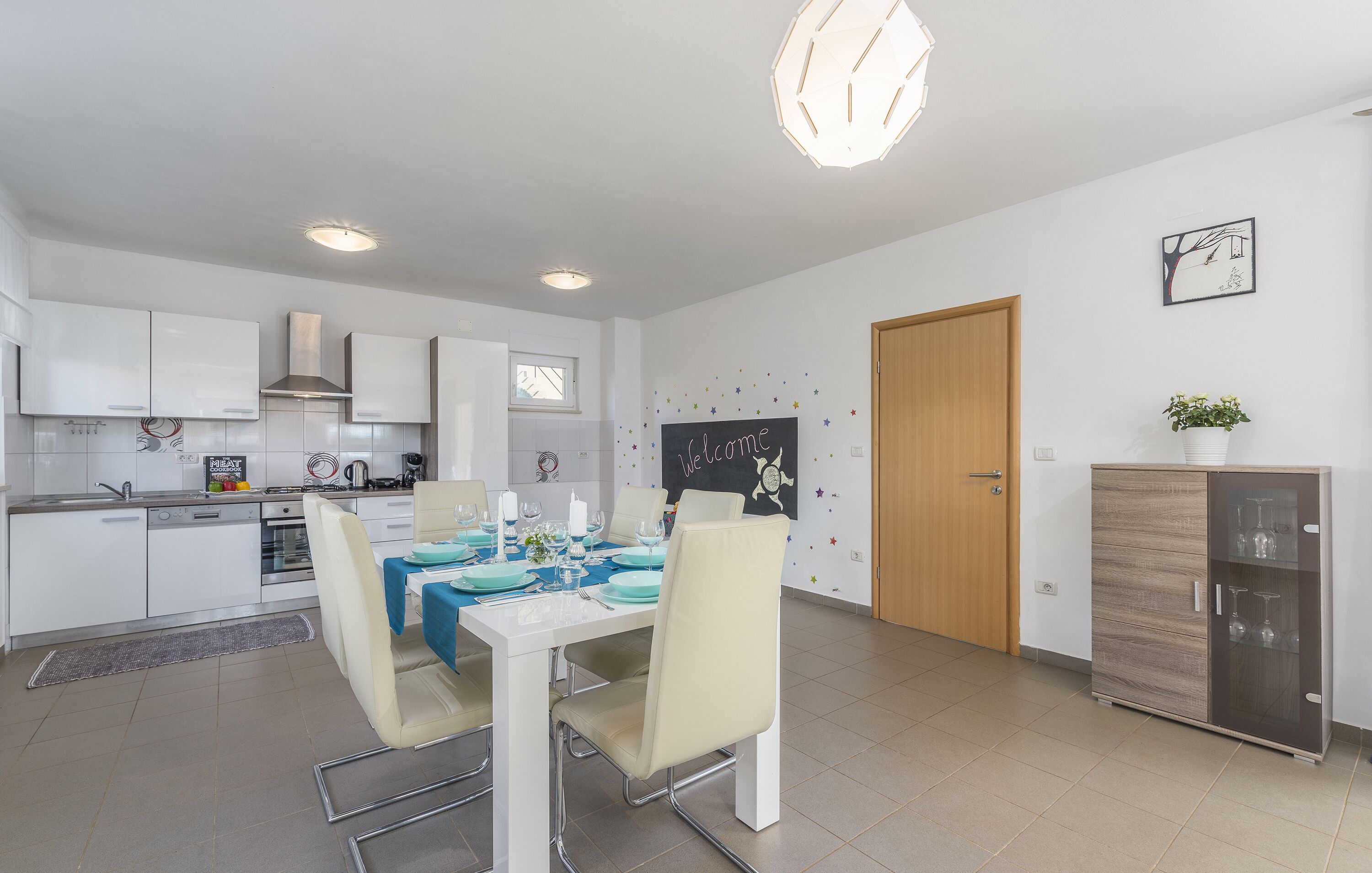 Una cocina moderna con armarios blancos, una mesa de comedor para cuatro personas y un horno empotrado.