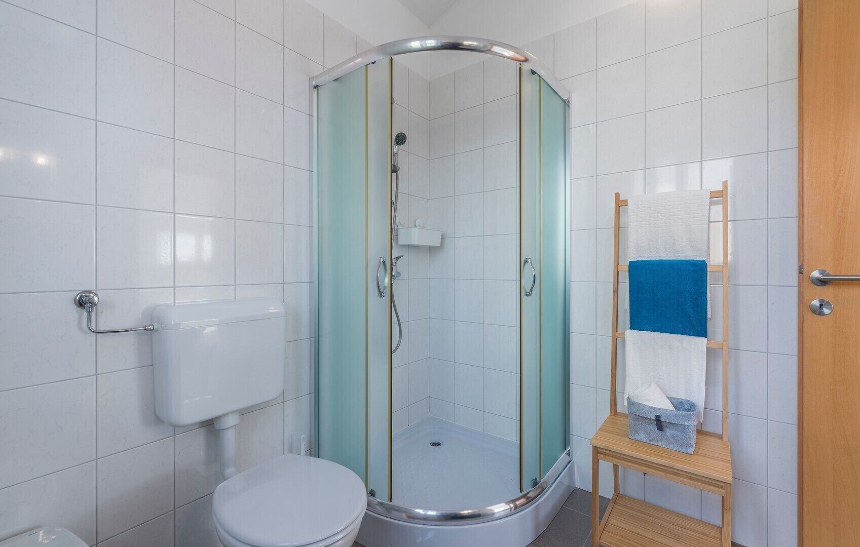 Een moderne badkamer met een douchecabine van glas, een toilet en een houten plank met handdoeken.