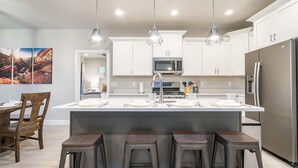 A modern kitchen with white cabinets, a central island with stools, a stainless steel refrigerator, and pendant lighting. - Zion Village Poolhouse (From $299) Sleeps 24 * Spa (Hurricane)
