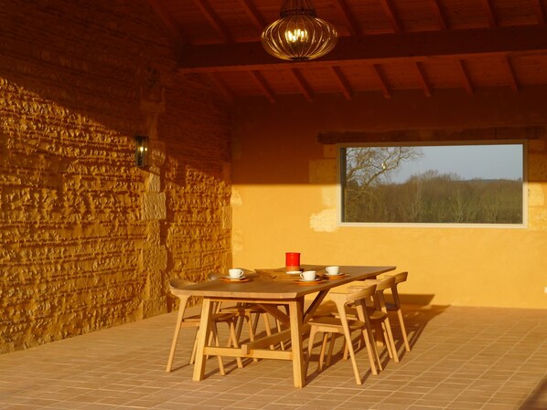 A wooden table with chairs, a window with a view of trees, and a stone wall.