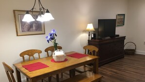 A dining area with a wooden table, four chairs, a bench, a vase with flowers, a lamp, a television on a stand, and a framed picture on the wall. - American Charm • King Bed & Kitchen Downtown (Cleveland)