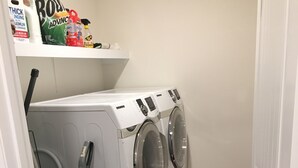 A laundry room with two front-loading washing machines, a vacuum cleaner, and a red rug on the floor. - American Charm • King Bed & Kitchen Downtown (Cleveland)