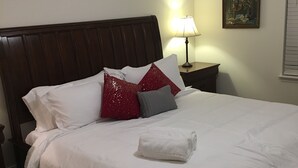 A neatly made bed with white and red pillows, a wooden headboard, a bedside lamp, and a painting on the wall. - American Charm • King Bed & Kitchen Downtown (Cleveland)