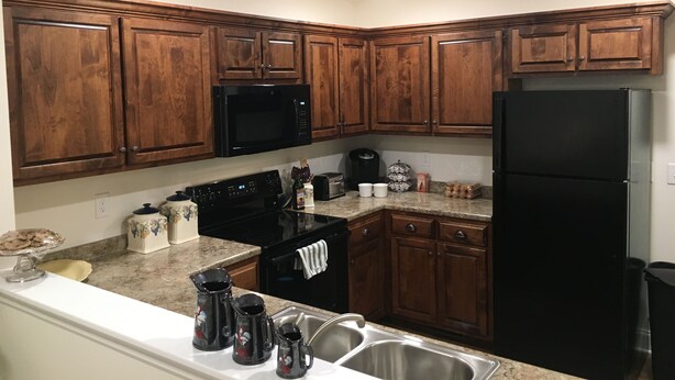 A kitchen with wooden cabinets, a black microwave, a black refrigerator, a coffee maker, and a sink. - American Charm • King Bed & Kitchen Downtown (Cleveland)