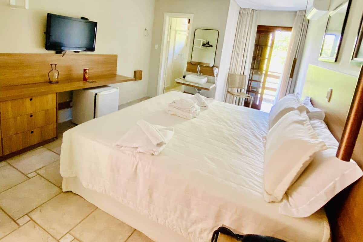 A hotel room with a bed, a desk, a television, and a bathroom visible through an open door.