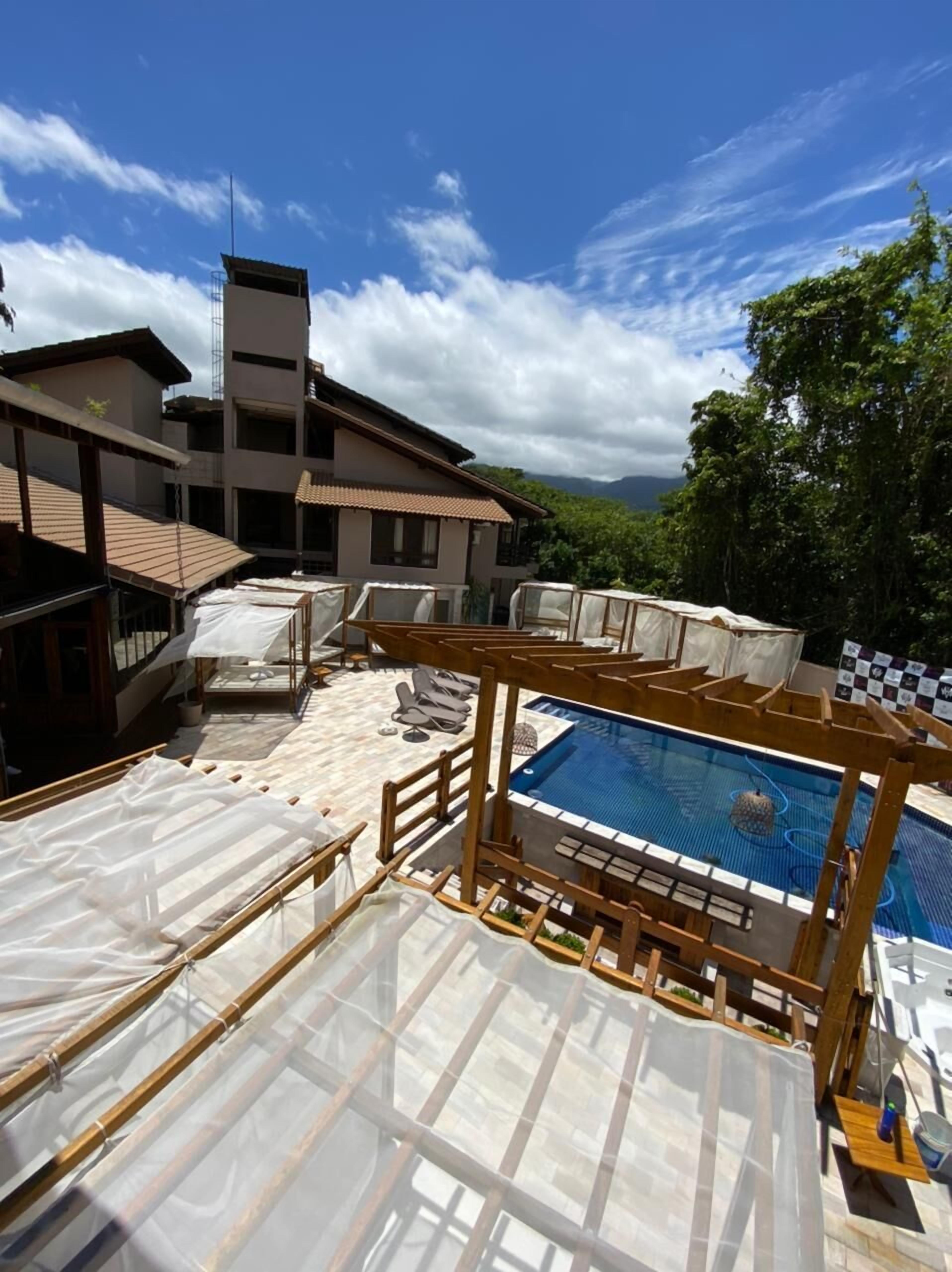 A rooftop pool area with sun loungers and a swimming pool, surrounded by buildings and trees.