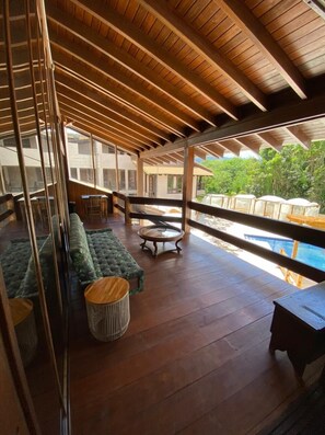 Un balcón amplio con suelo de madera, un espacio de descanso acolchado y vistas a una piscina.