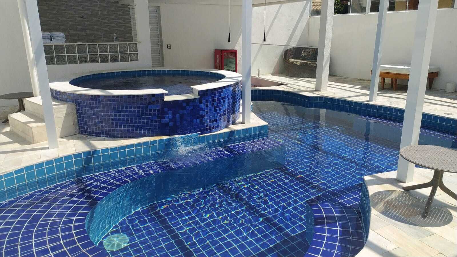 A swimming pool with a hot tub, tiled in blue, and a small table and chair nearby.