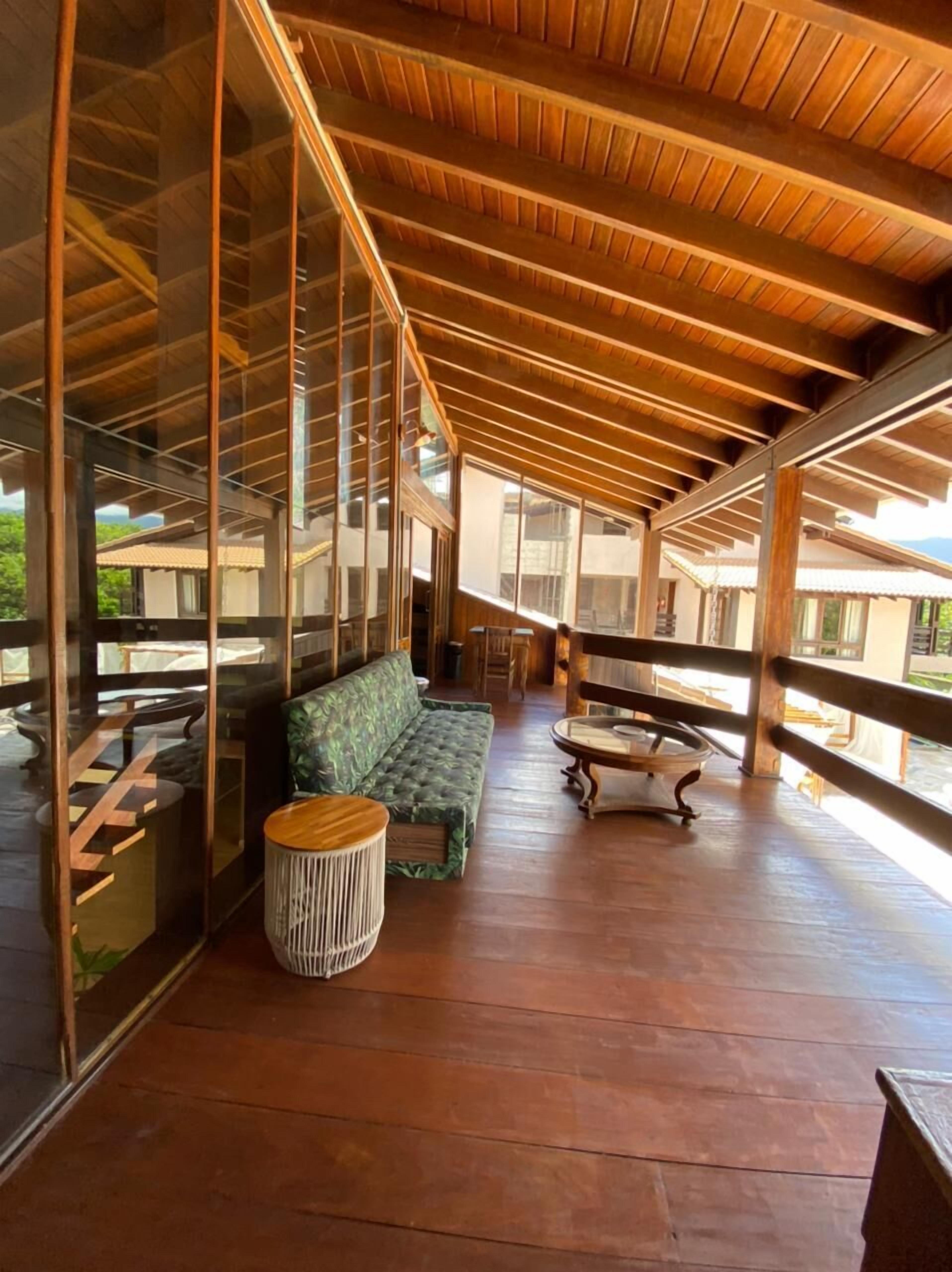 A covered outdoor seating area with wooden flooring, a cushioned bench, and a round table.