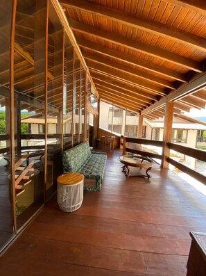 Un área de estar al aire libre techada, con piso de madera, un banco acolchado y una mesa redonda.