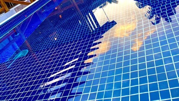 Piscina com superfície revestida de azulejos refletindo o céu e as estruturas ao redor.
