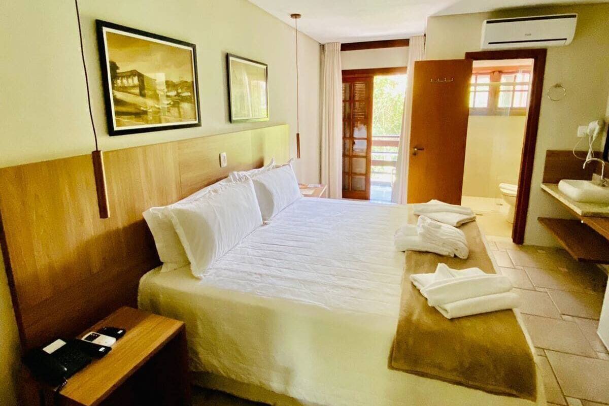 A hotel room with a bed, a bedside table, a bathroom with a sink, and a door leading to an outdoor area.