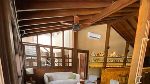 Uma sala de estar aconchegante com sofá, mesa de centro, luminária e um espaço bar com prateleiras cheias de garrafas.